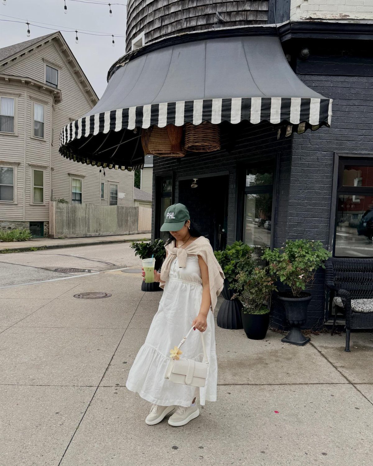 A woman in a long white dress and white sneakers standing on a city sidewalk.