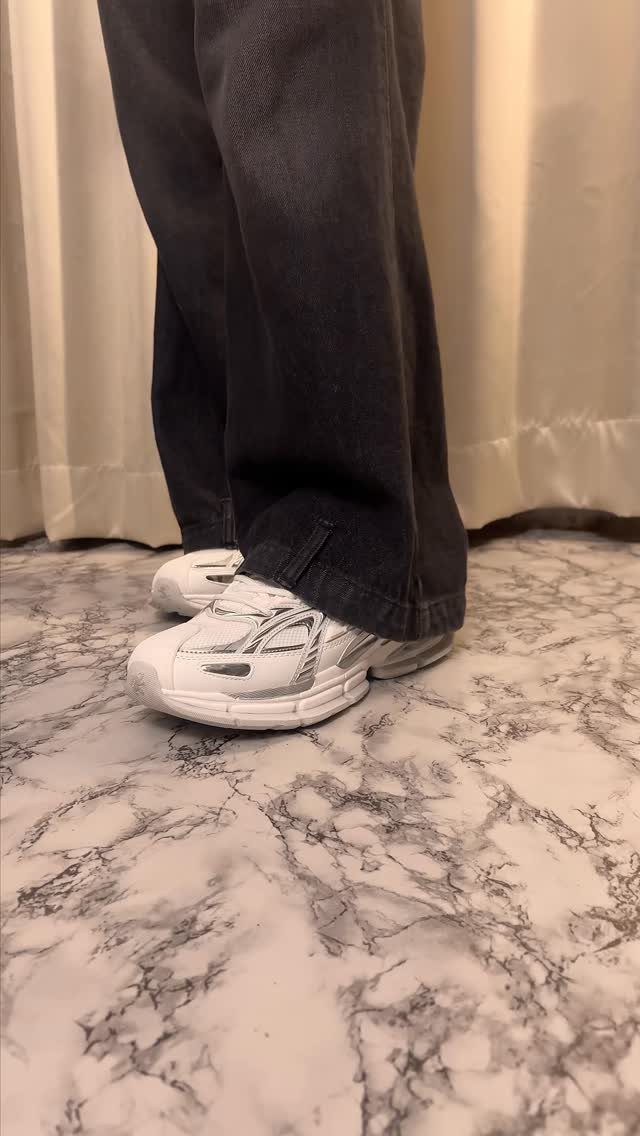 White chunky sneakers worn with dark denim jeans on a marble floor.