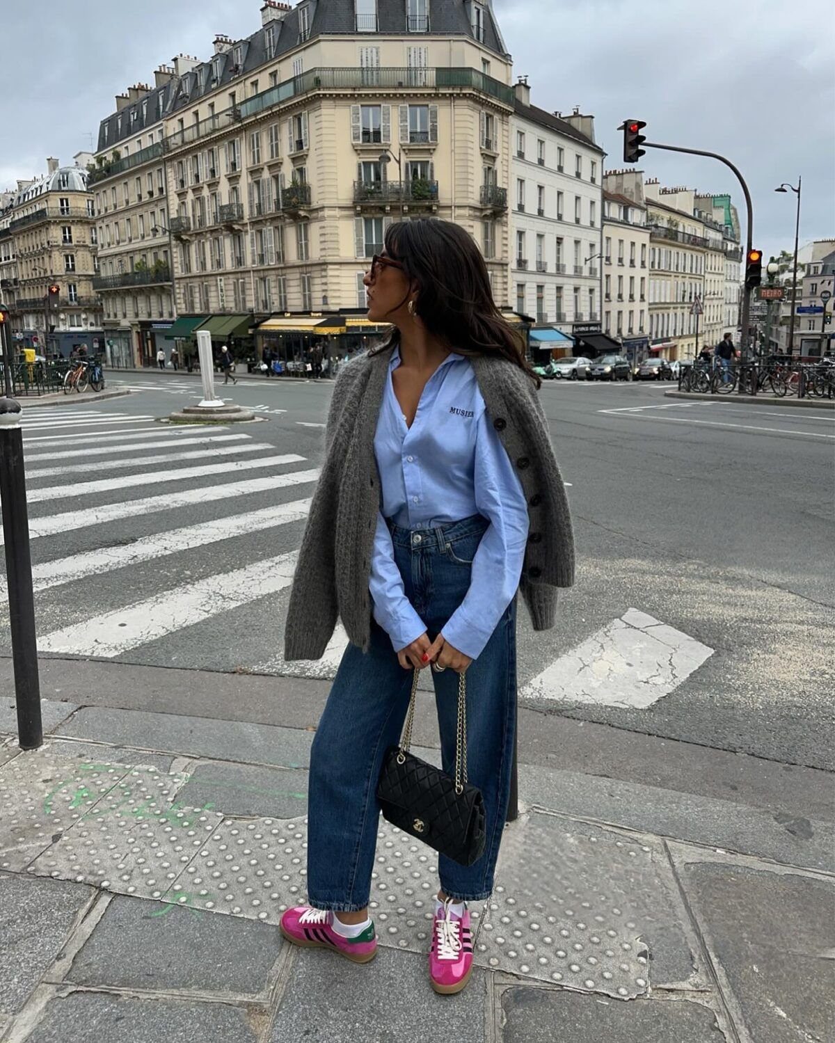 Woman wearing blue jeans and bright pink colorful sneakers standing on a city street corner.