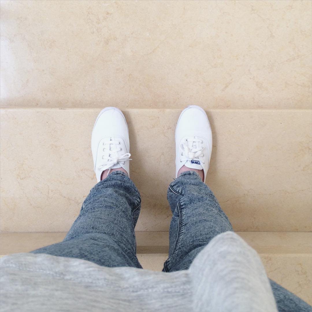 White sneakers paired with blue denim jeans and a grey sweater on beige stairs.
