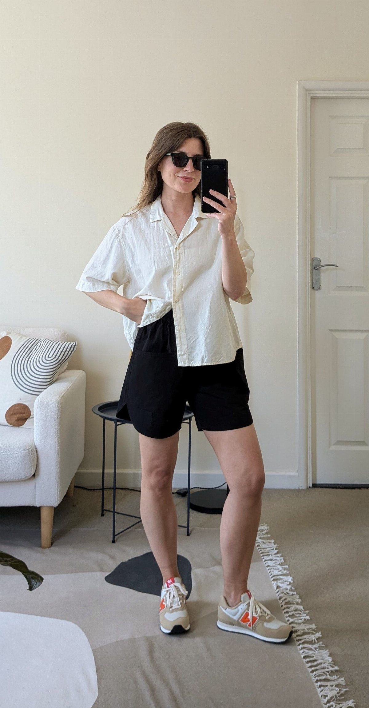 Woman in white shirt and black shorts posing in chunky white and orange sneakers.