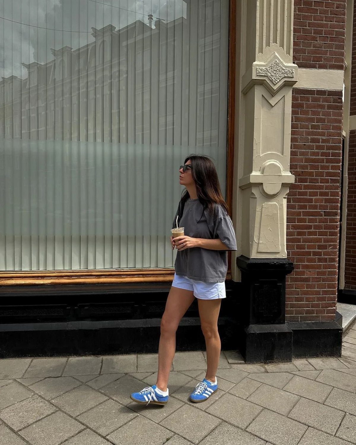 Woman in grey t-shirt and white shorts walking while wearing blue sneakers.