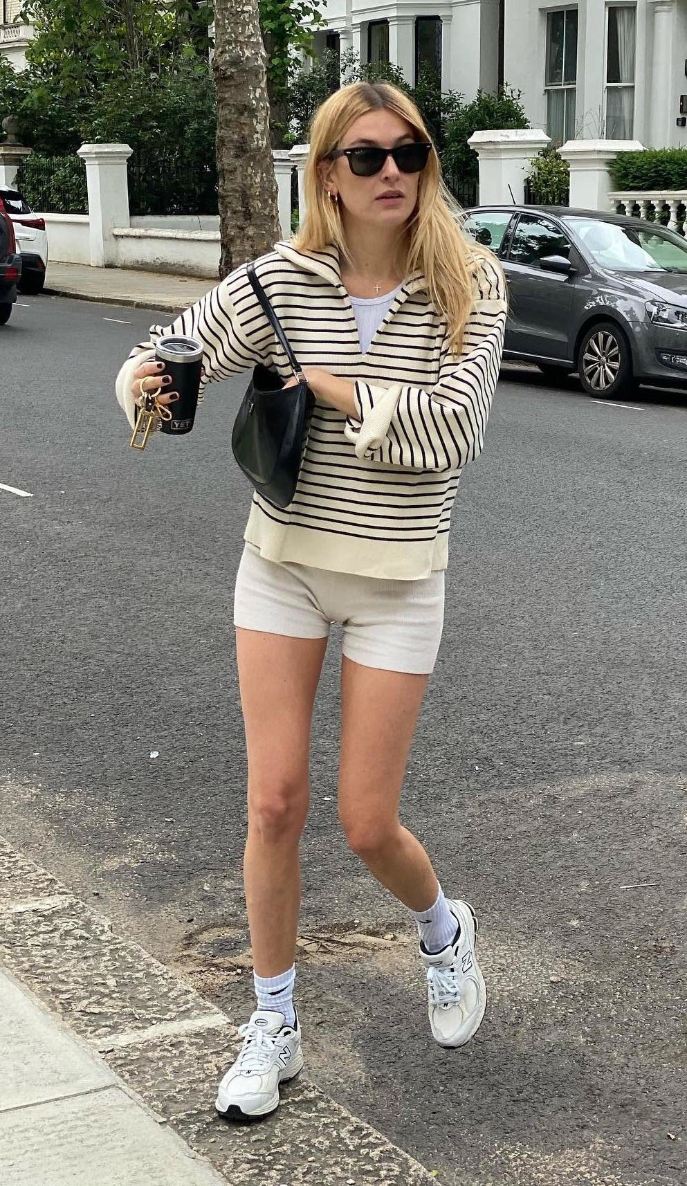 A blonde woman walking down a city street wearing white shorts and white sneakers.