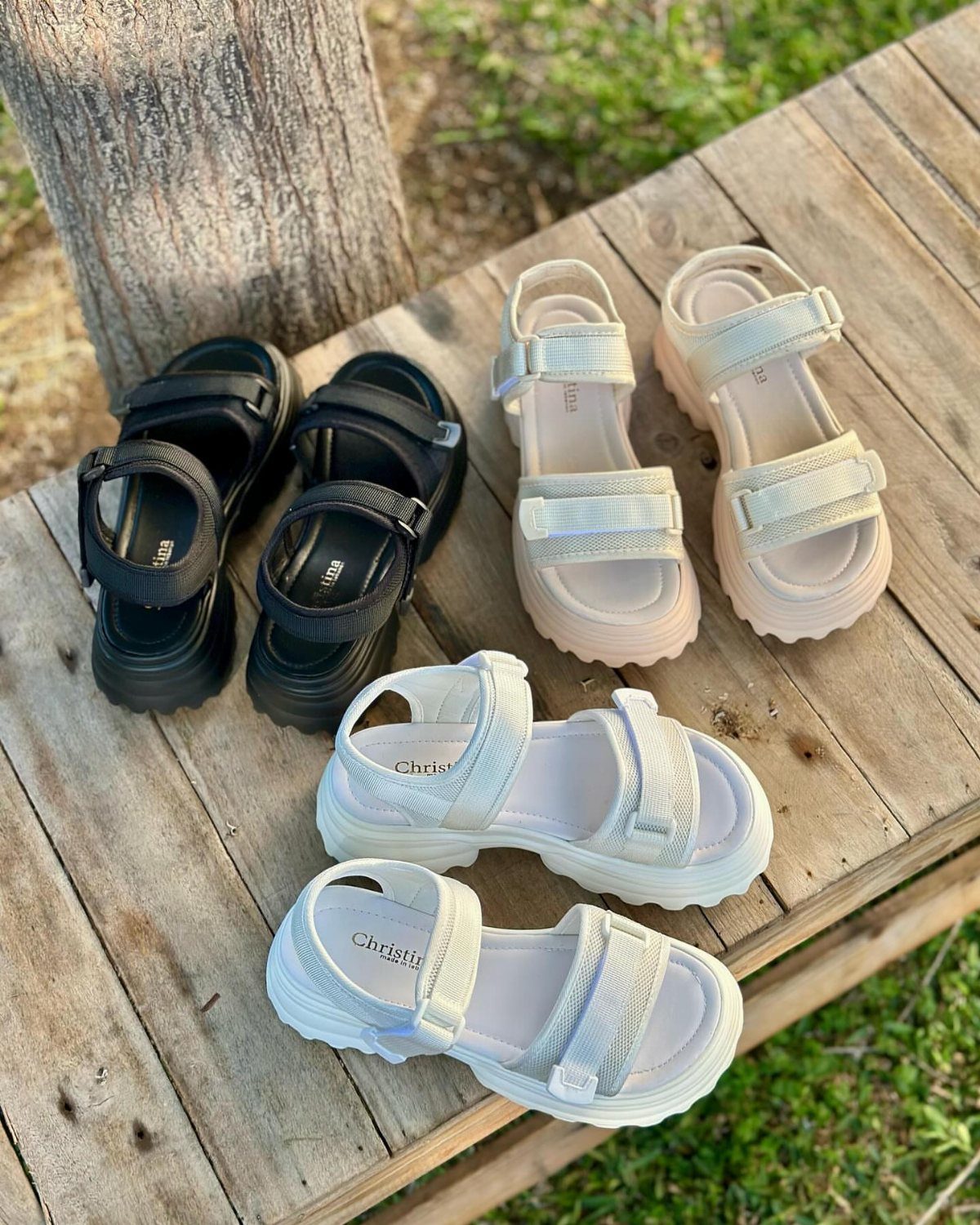 Three pairs of platform sandals in black, cream, and white resting on a wooden bench.