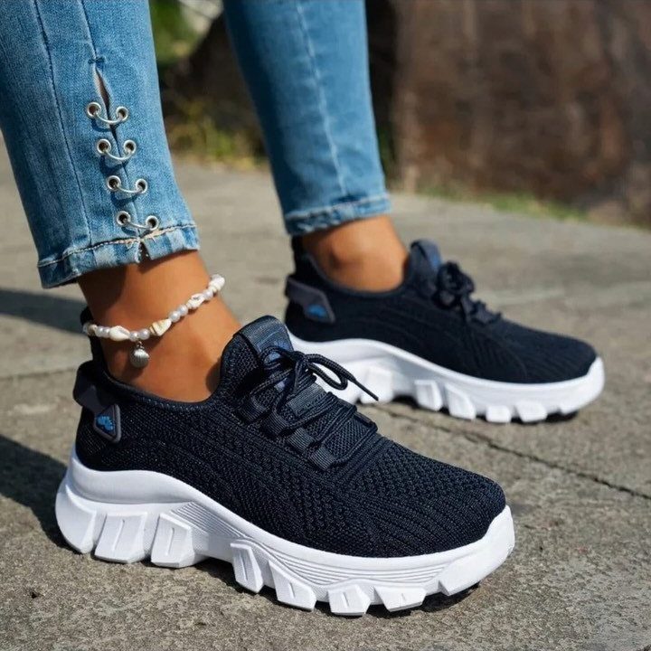 Black mesh sneakers with thick white soles worn by a person in blue jeans.