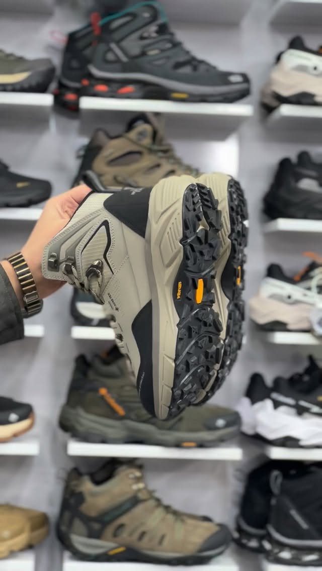 A hand holds a hiking boot showing the heavy-duty lugged rubber outsole in a shoe store.