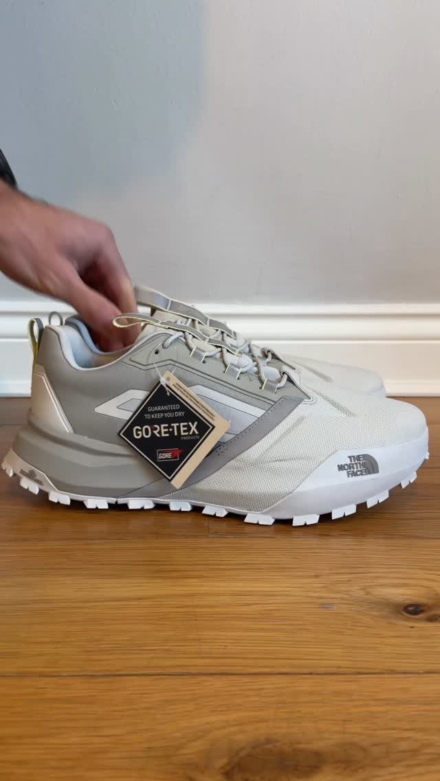 A light grey Gore-Tex sneaker with a white chunky sole resting on a wooden table.