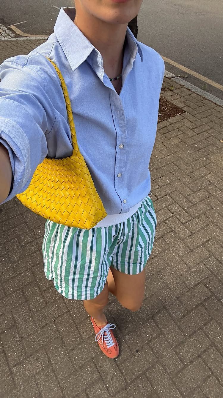 Person standing on a brick sidewalk wearing striped shorts, a blue shirt, and orange sneakers.