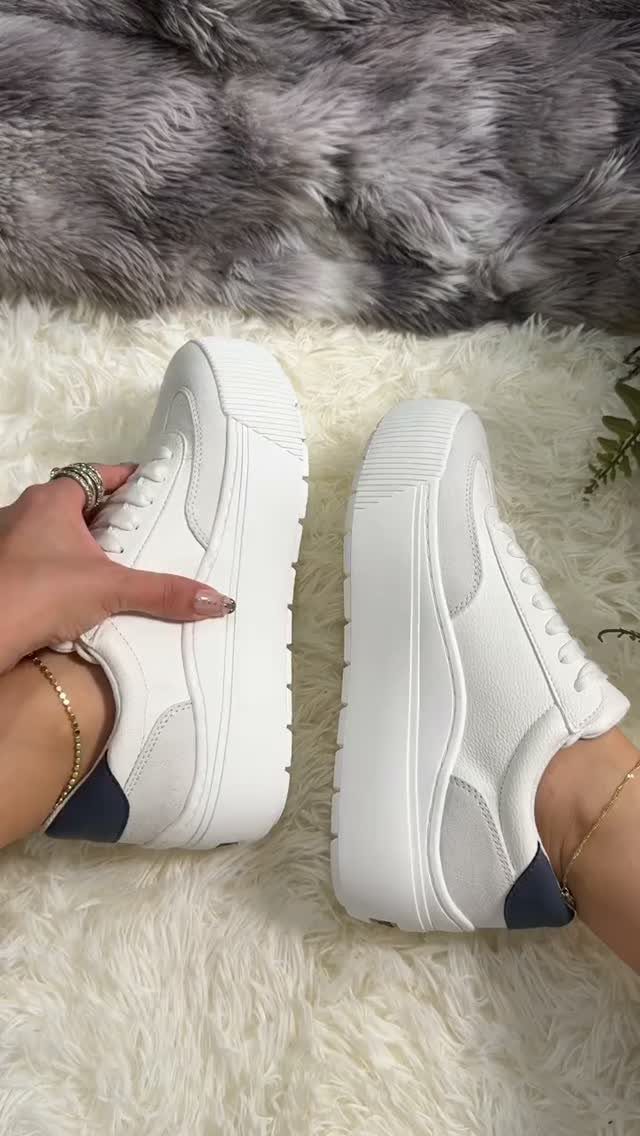 White platform slip-on sneakers with navy heel accents held against white faux fur.