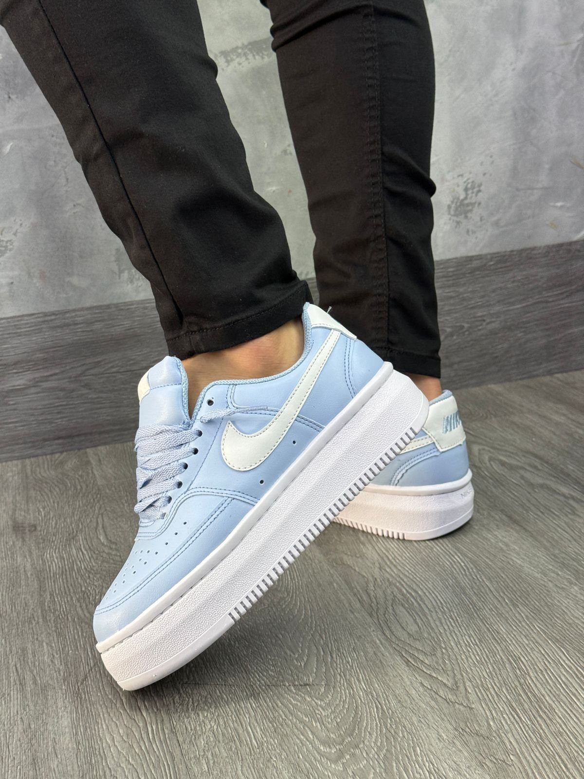 Light blue Nike platform sneakers worn by a person in black pants on a grey floor.