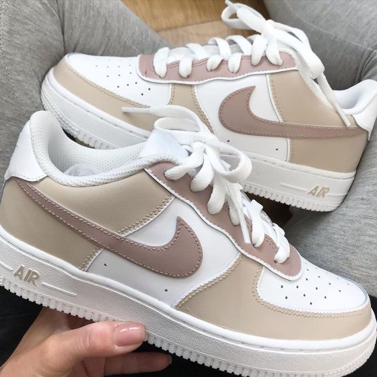A hand holding a pair of beige and white Nike Air Force 1 sneakers.