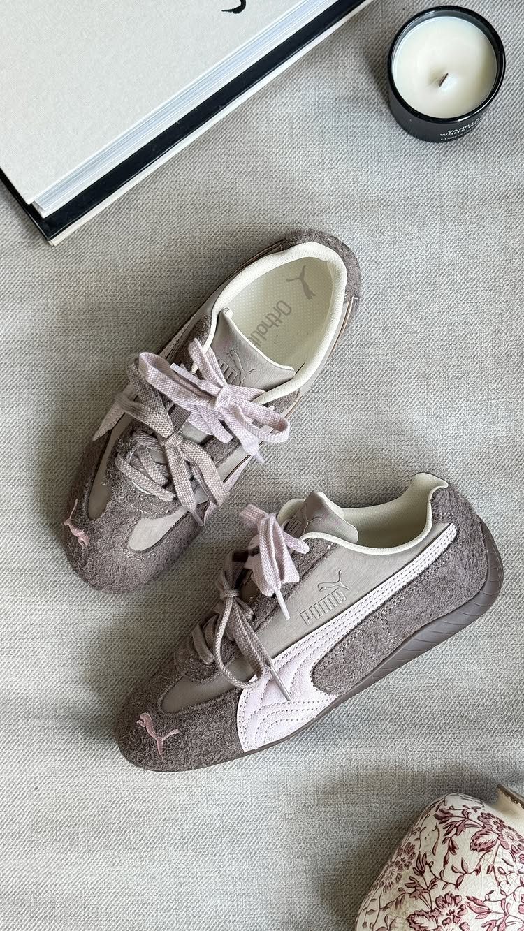 Grey and pink suede Puma Speedcat sneakers resting on a textured grey fabric surface.