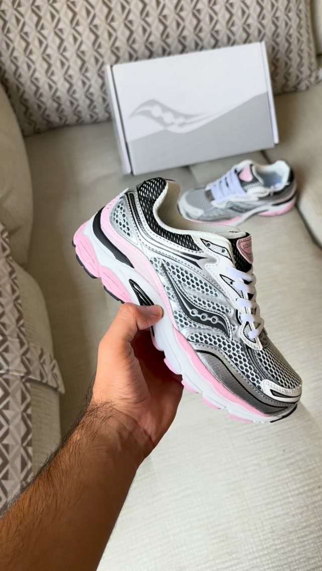 A hand holds a silver and pink athletic running shoe near its shoebox.