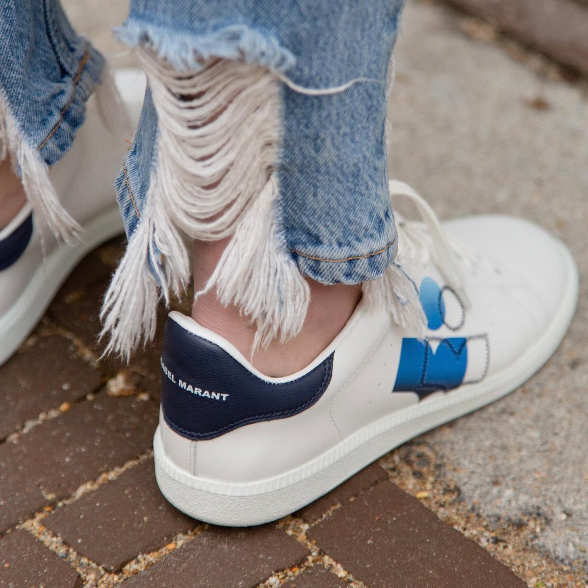 White leather sneakers with blue details worn with distressed blue denim jeans.