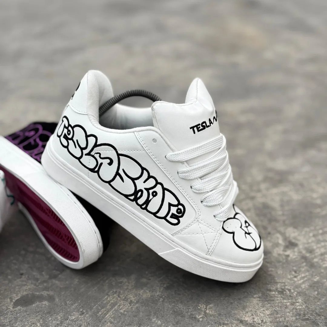 White low-top sneakers with black graffiti-style lettering resting on a grey concrete ground.