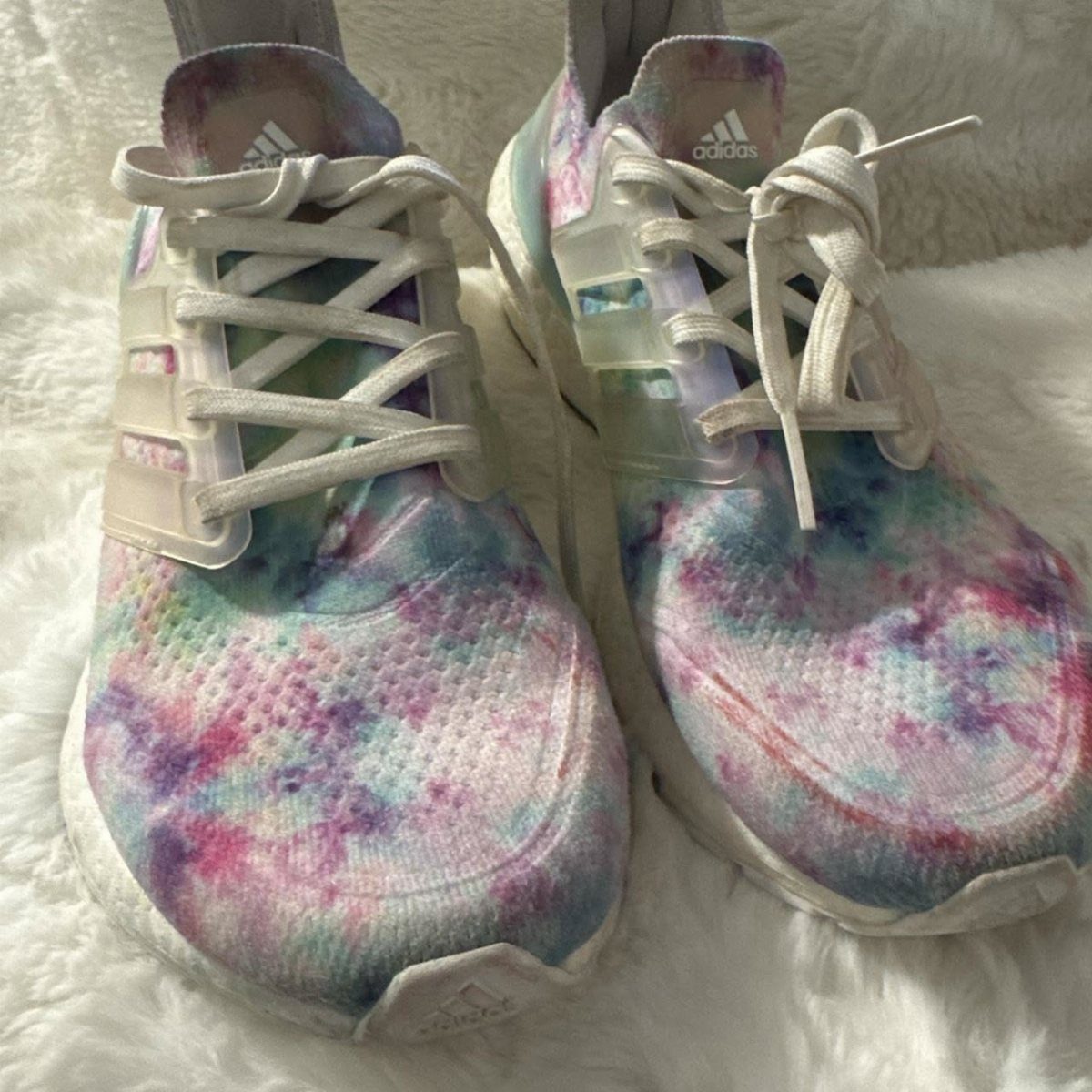 Tie dye patterned Adidas athletic shoes with white laces on a white fuzzy surface.