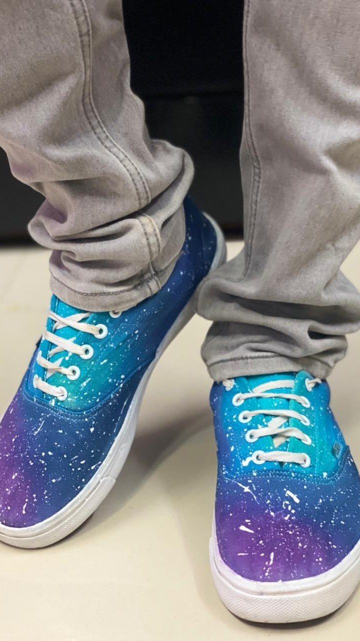 Person wearing grey sweatpants and blue galaxy-patterned canvas sneakers with white star splatters.
