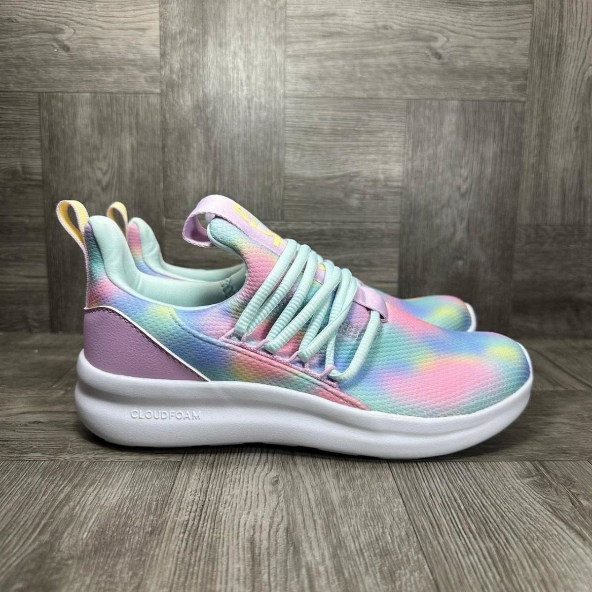 Tie-dye patterned athletic shoes with pastel colors resting on a grey wooden surface.