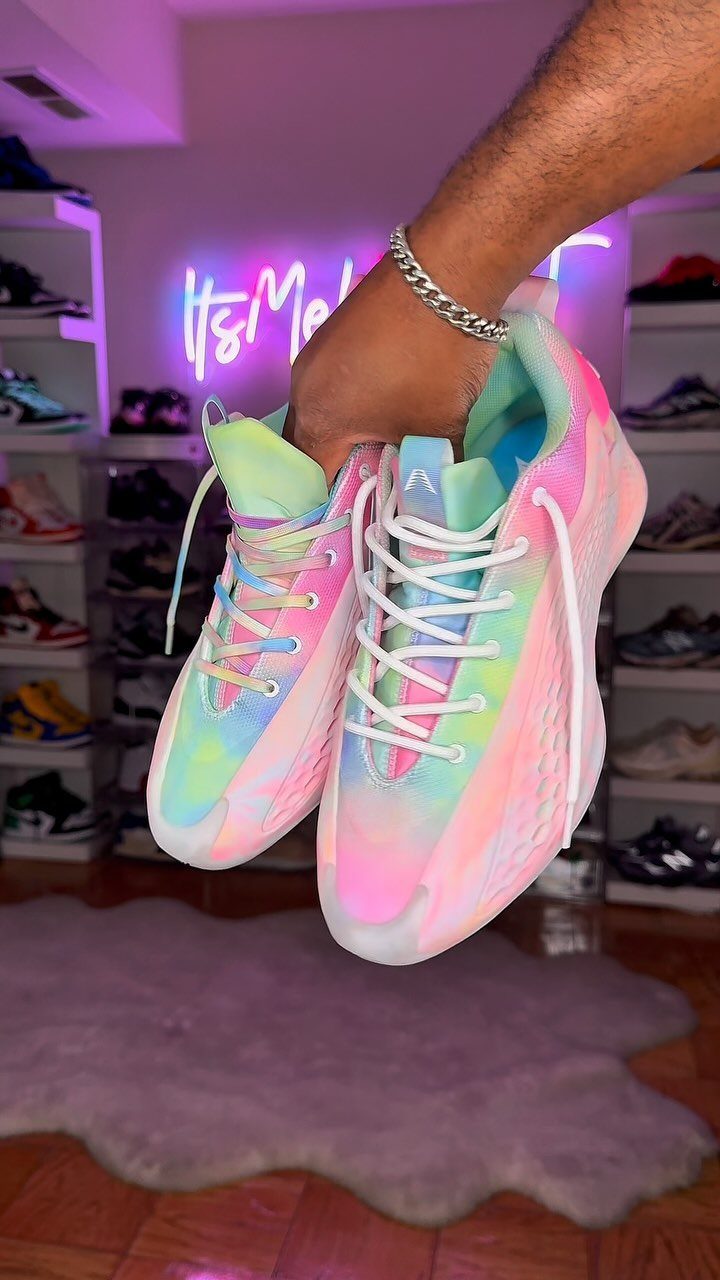 A hand holds up a pair of colorful pastel tie-dye athletic running shoes.