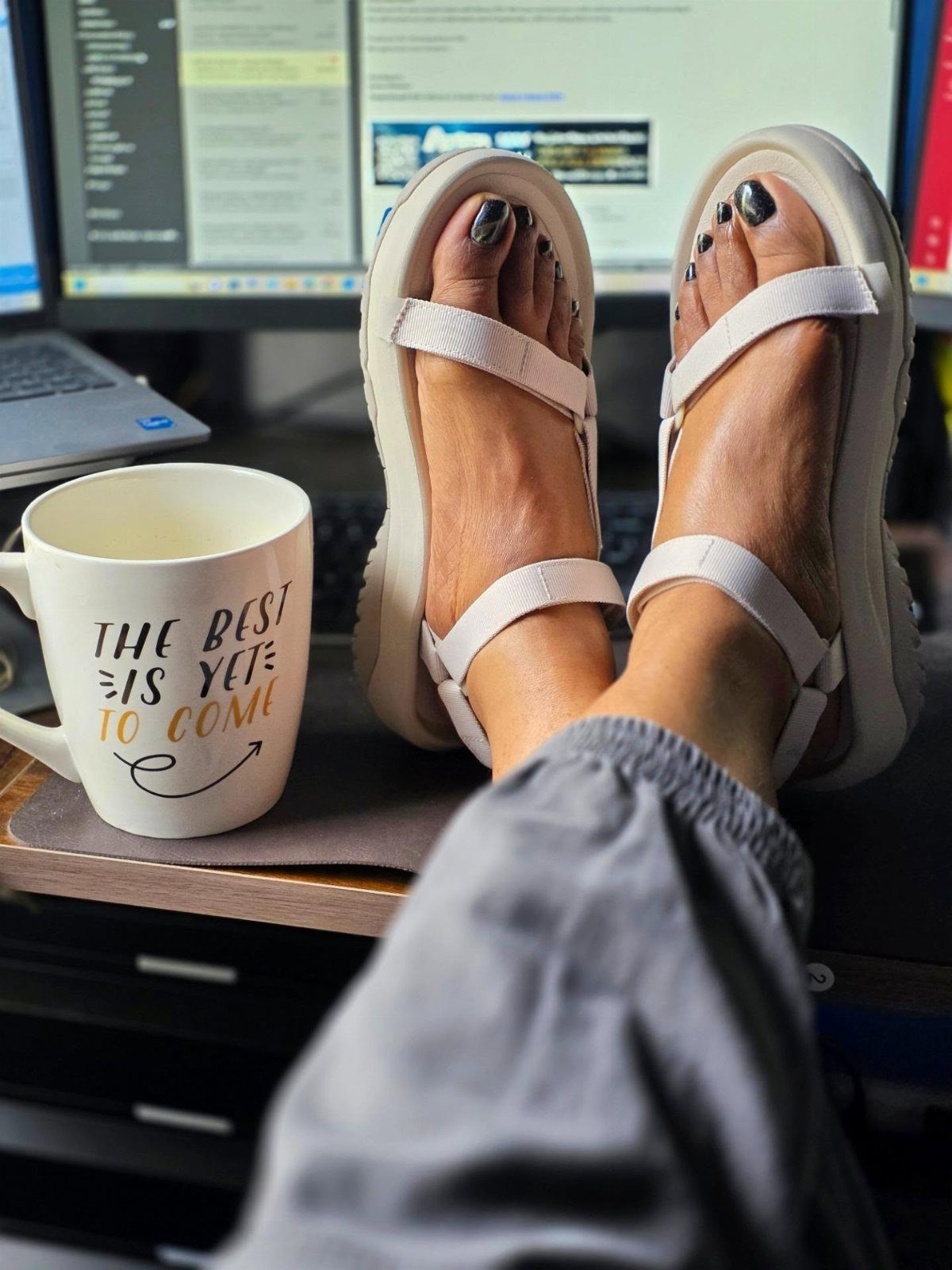 White strappy chunky sandals worn by a person resting their feet on a desk.