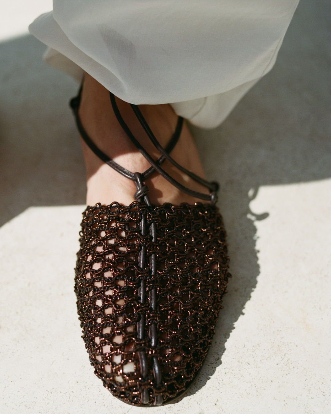 Brown mesh closed-toe flat sandals with thin black straps worn on a person's foot.