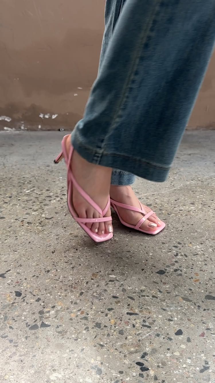 Pink strappy kitten heel sandals worn by a person in blue denim jeans on concrete.