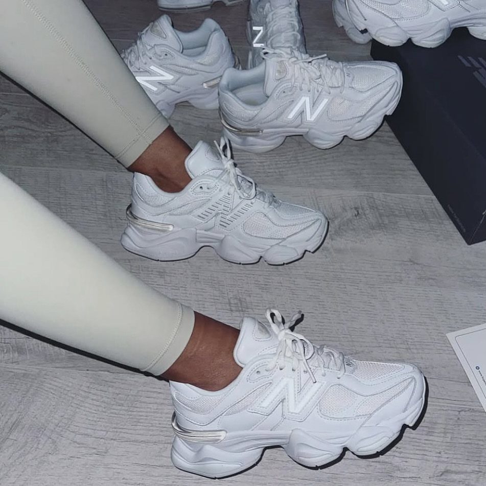 Person wearing chunky white New Balance sneakers and white leggings on a wooden floor.