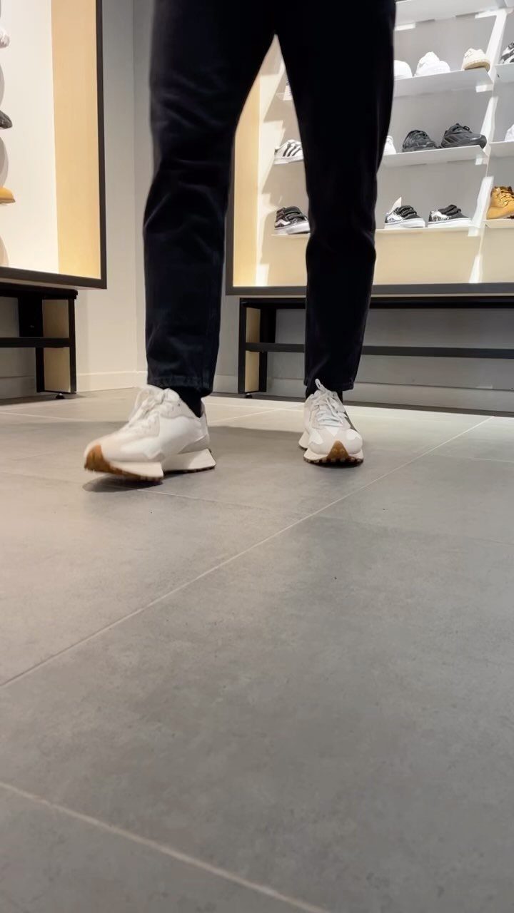 Person wearing white leather and mesh sneakers and black trousers standing in a shoe store.
