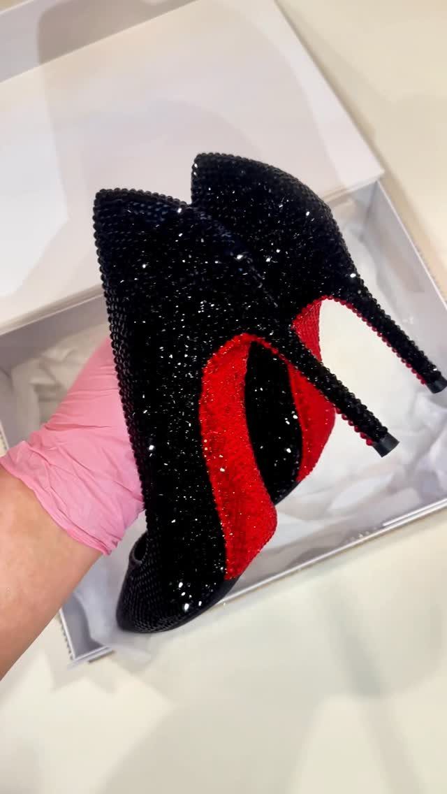 Black crystal-encrusted high heels with red soles being held in a white box.