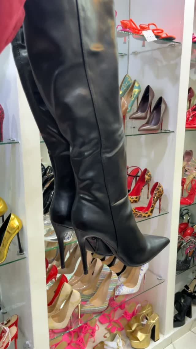 Black leather high-heeled stiletto boots displayed on a shelf among other footwear.