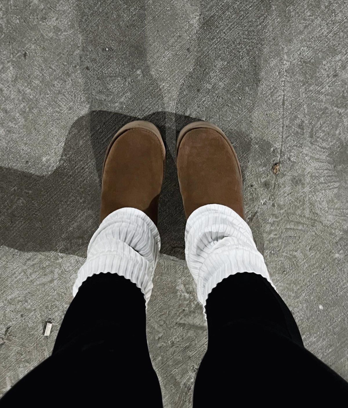 Tan Ugg boots paired with white knit leg warmers and black leggings on concrete.