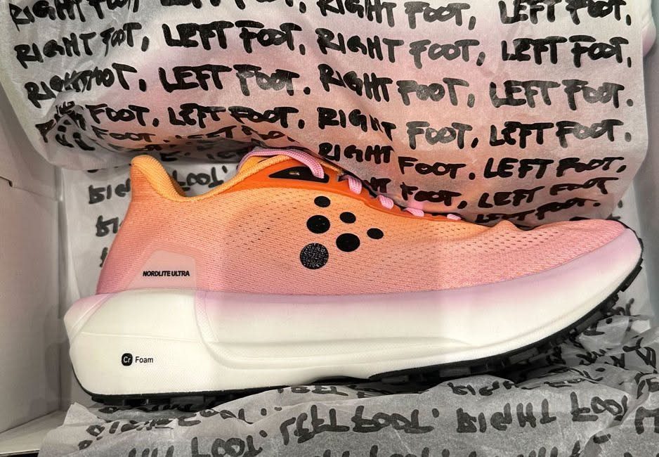 A pink and orange athletic running shoe resting on patterned tissue paper.