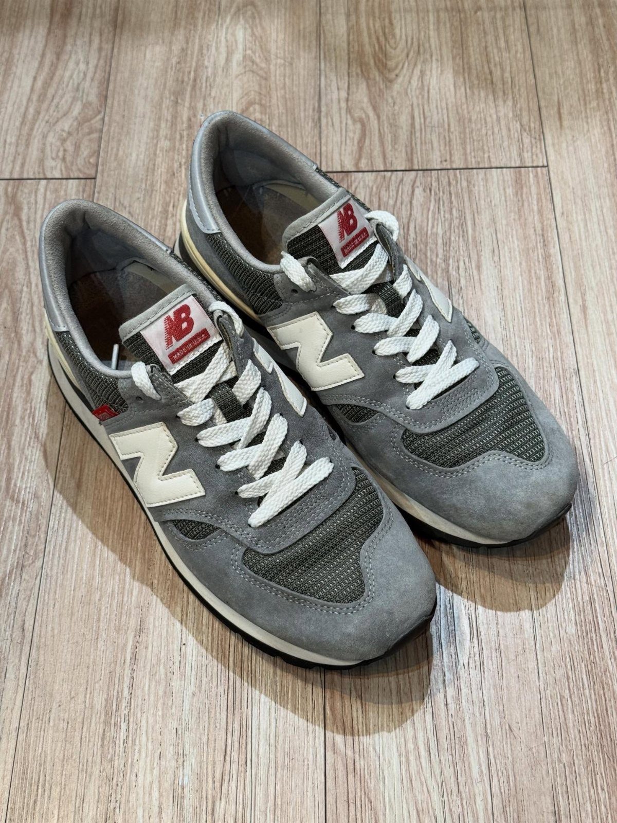 Grey New Balance athletic shoes with white laces resting on a light wooden floor.