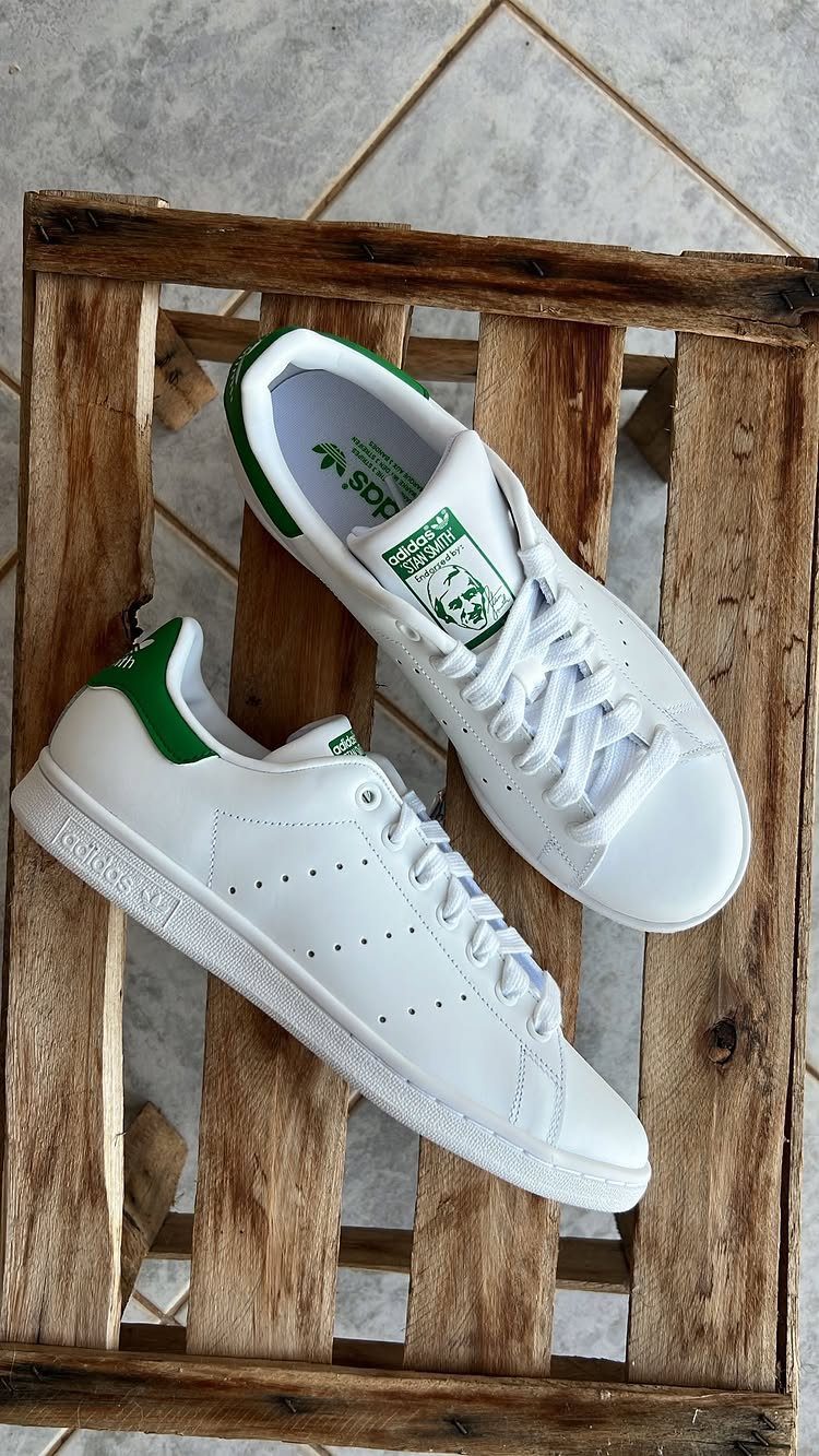 White Adidas Stan Smith sneakers with green heel tabs resting on a wooden crate.