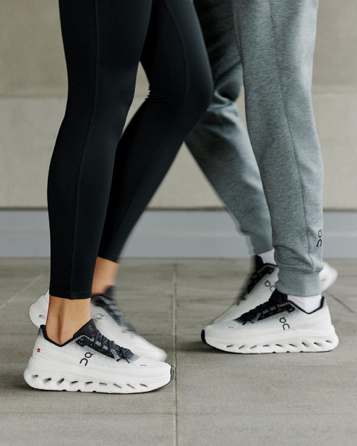 Two people walking outdoors wearing white On Cloudtilt sneakers and athletic clothing.