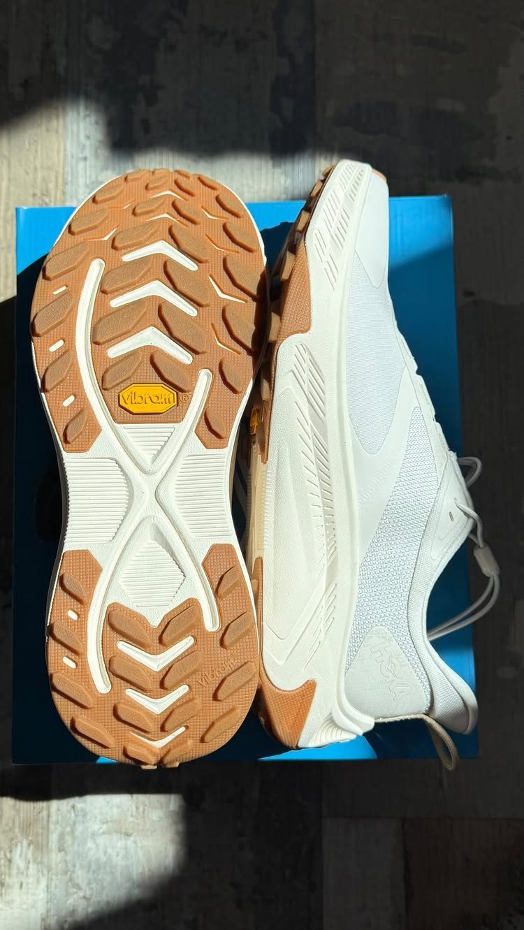 White athletic walking shoes with tan Vibram soles resting on a blue box.