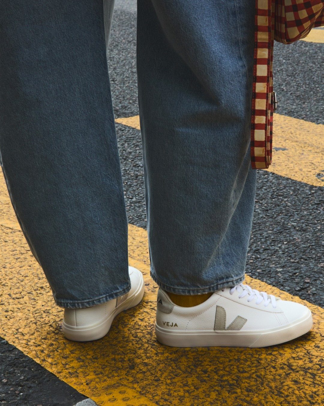 White Veja Campo sneakers worn with blue denim jeans on a street with yellow markings.