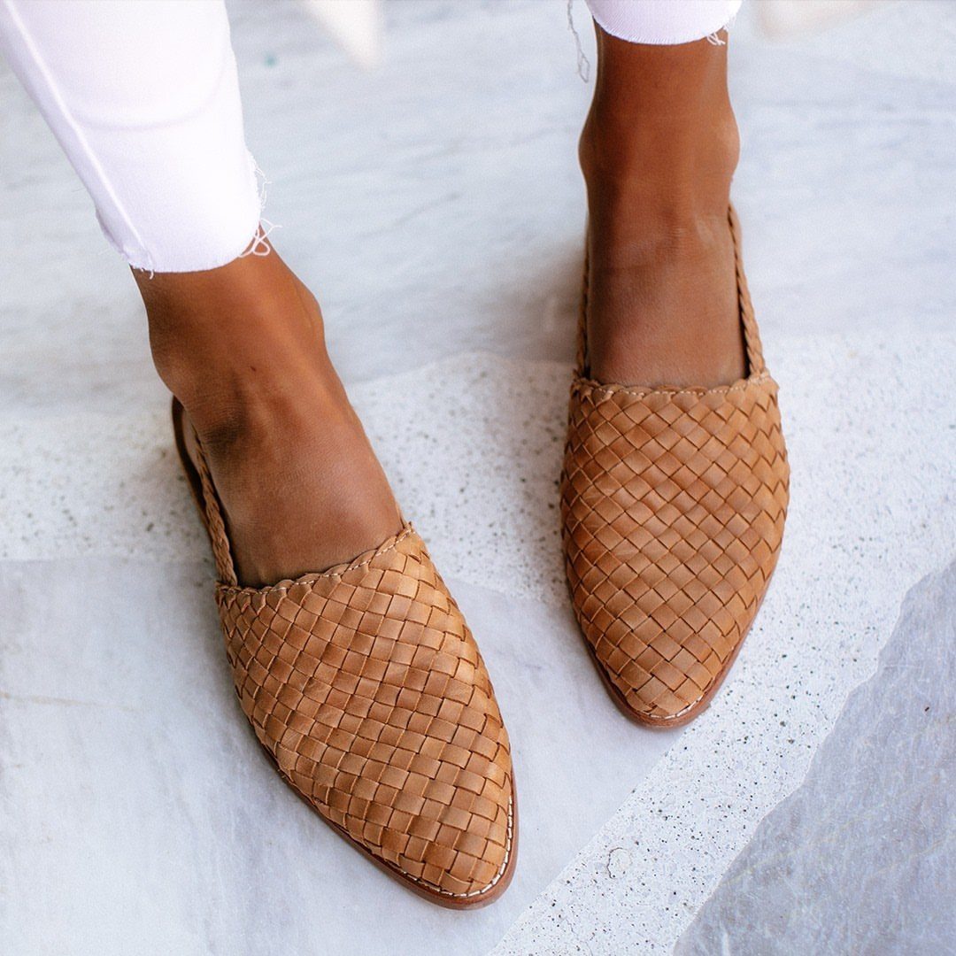 Tan woven leather flats worn by a person standing on white marble.