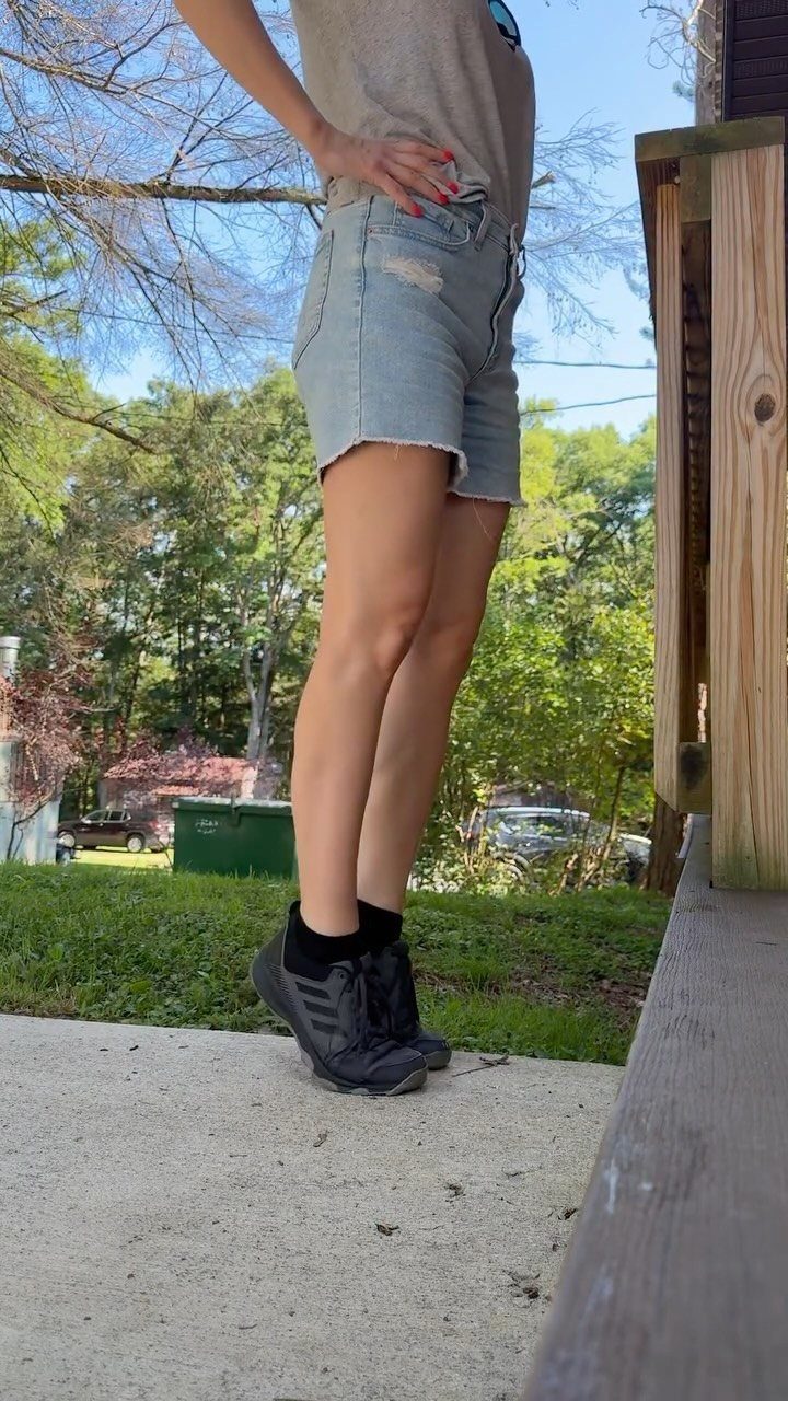 A woman standing outdoors wearing black zero drop sneakers and black socks on concrete.